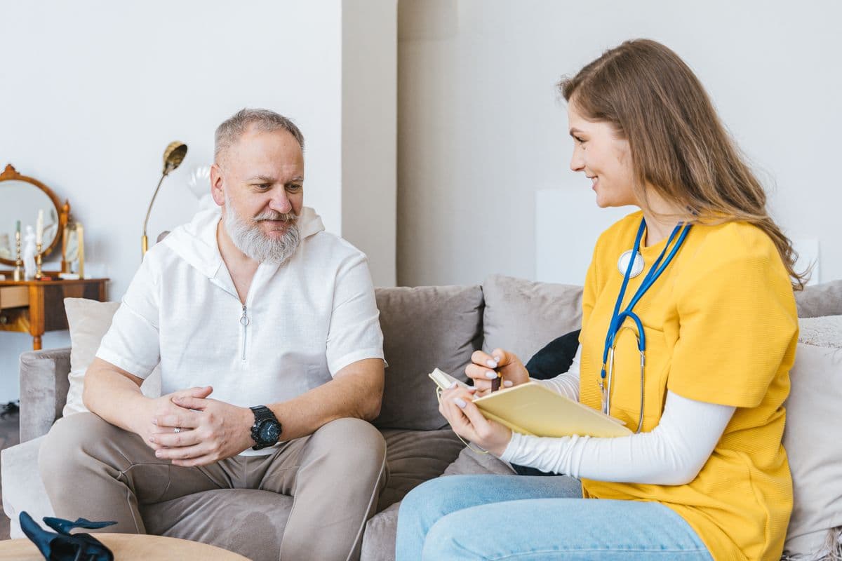 Een zorgprofessional in gesprek met een oudere man, beiden lachend